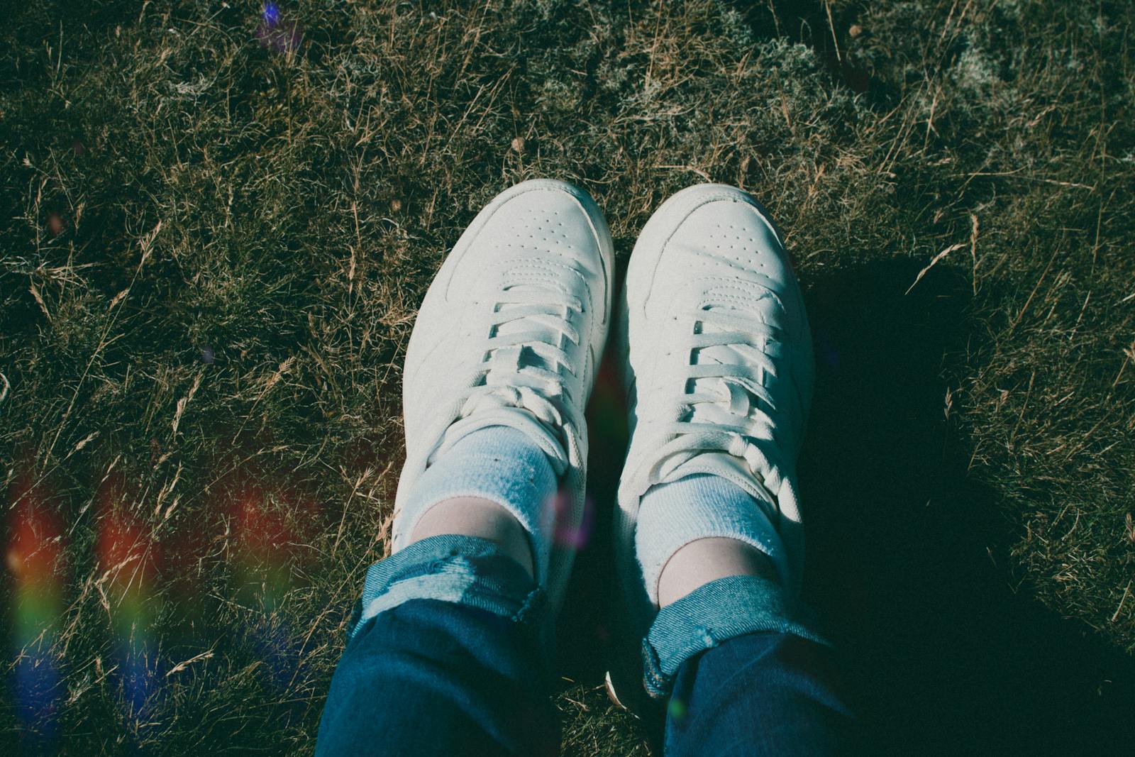 Top view of white sneakers and jeans on grassy field, natural sunlight.