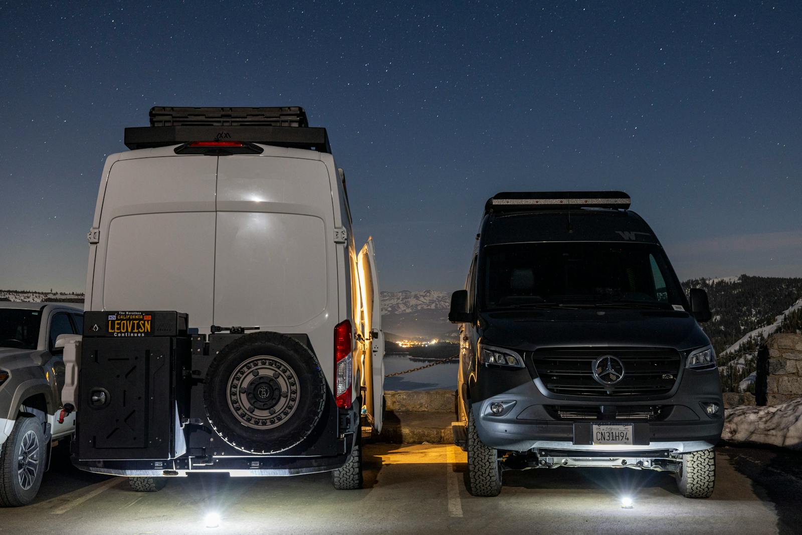 Two camper vans parked under a starry night sky in a winter landscape.