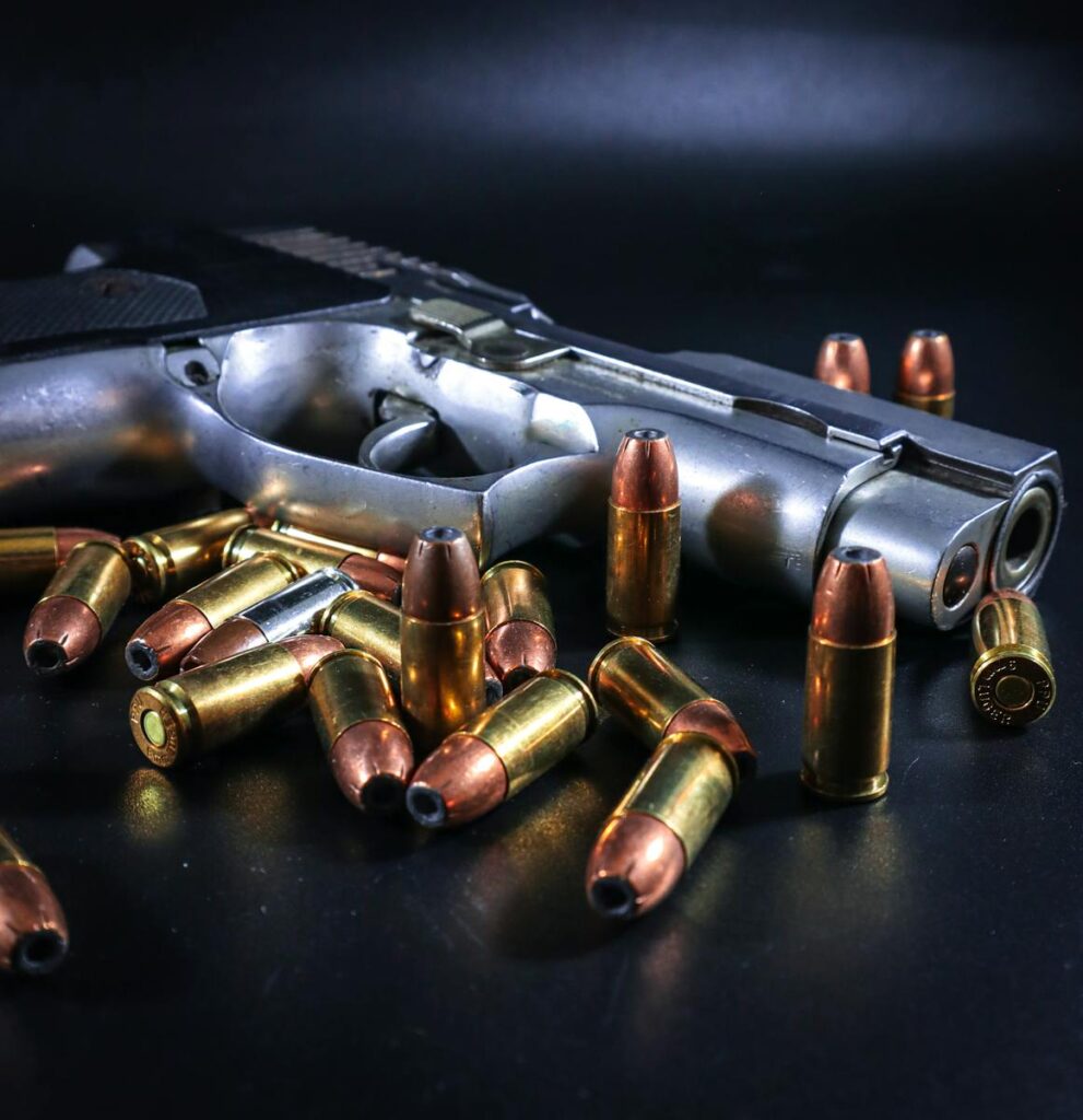 The Great Debate: 9mm vs. .45 ACP for Self-Defense and Carry Silver handgun with scattered bullets on dark background, emphasizing danger and weaponry.