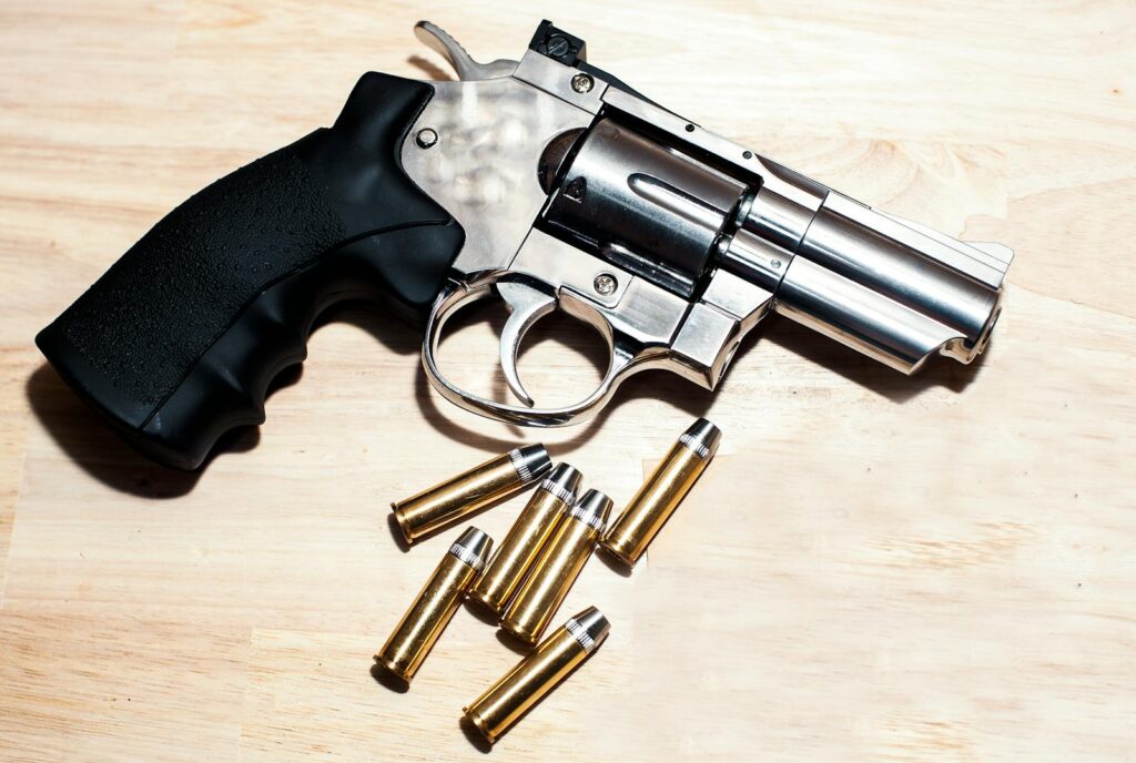 Silver revolver and bullets on a wooden surface illustrating security themes.