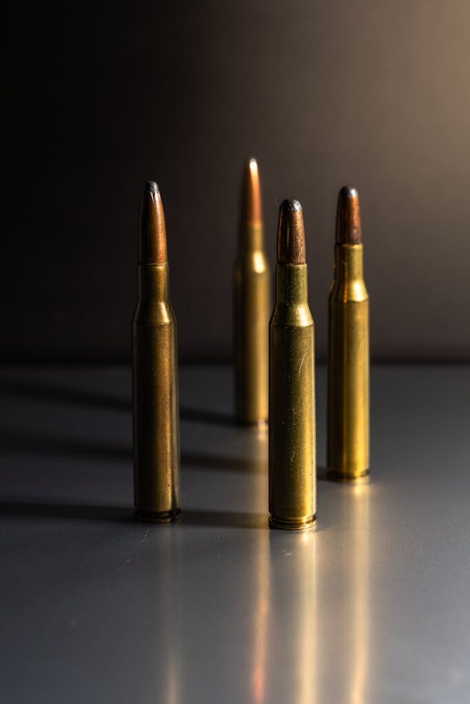 Four brass bullets standing upright on a reflective surface with soft lighting.
